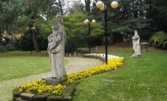 Giardino | Costruito all’italiana dai Conti Taverna e trasformato in parte all’inglese dai Marchesi Isimbardi, appassionati di botanica, vi si trovano tassi, magnolie sempreverdi, faggi, ippocastani ed un gigantesco platano, oltre a specie esotiche come aceri giapponesi, pini Himalayani ed un Ginkgo Biloba, di moda nei giardini dell’Ottocento. Alcune statue novecentesche richiamano le attività del territorio, industria e agricoltura. Qui è apprezzabile la facciata interna del Palazzo in stile neoclassico, di Giacomo Tazzini. Il muro con il confinante Palazzo Diotti, sede della Prefettura, era attraversabile un tempo tramite due porte, usate si dice da Benito Mussolini per concedersi brevi evasioni e di sicuro per fuggire dalla città il 25 aprile 1945. Adiacente al giardino è la “Torre delle sirene”, reperto della II Guerra Mondiale: torre di allarme dal caratteristico tetto conico in acciaio, rifugio antibomba per le autorità.